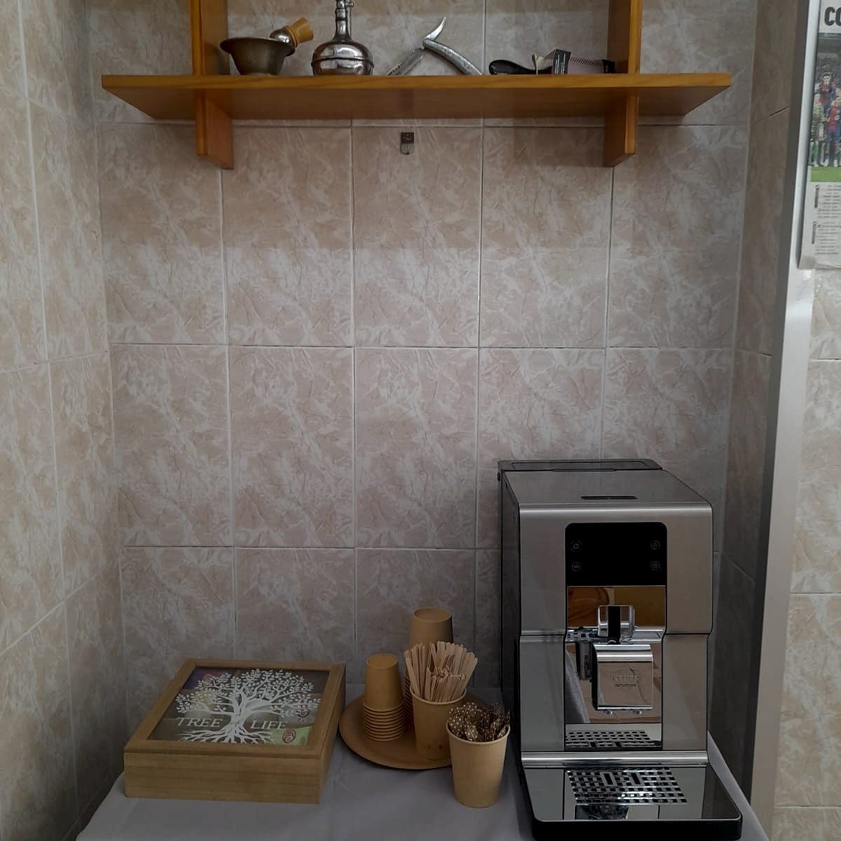 Rincón de la tertulia: máquina de café, caja de tés y utensilios vintage en estantería de madera.