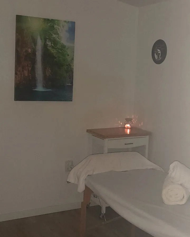 Cabina de quiromasaje en Peluquería Juan — camilla, velas y cuadro de cascada en ambiente cálido